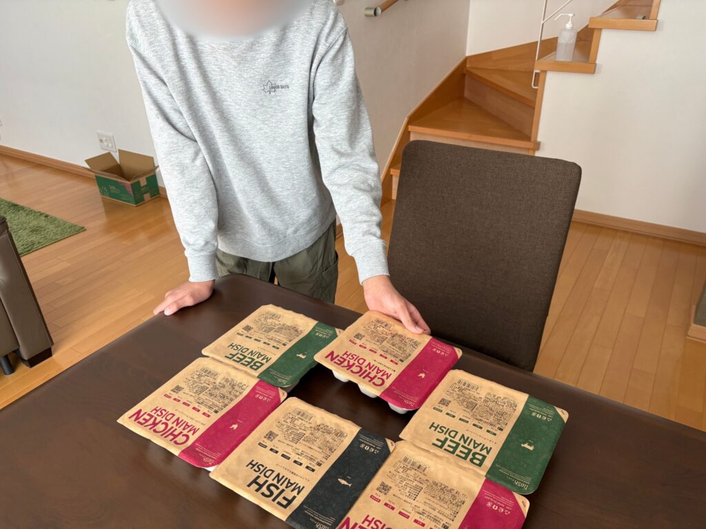 ナッシュの冷凍弁当6食分のパッケージを子どもがダイニングテーブルに並べている写真
